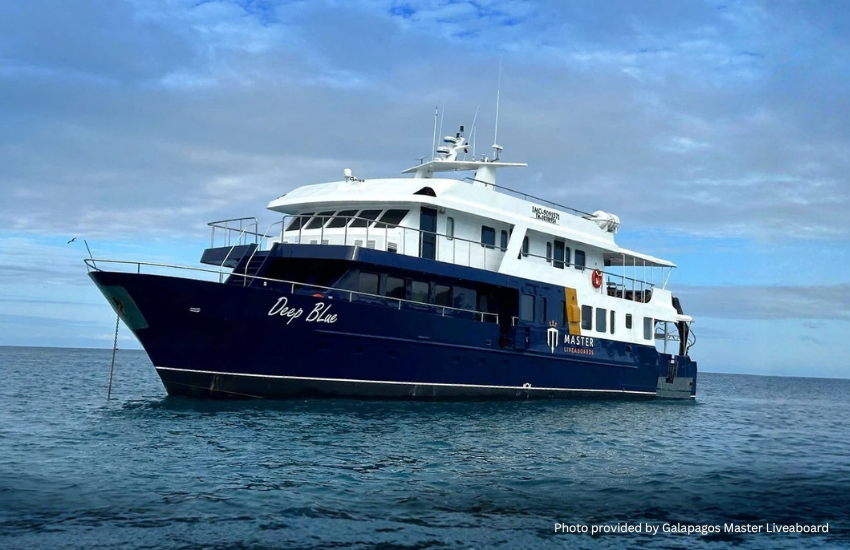 The Deep Blue vessel from the Galápagos Master fleet anchored in calm blue water under a cloudy sky.