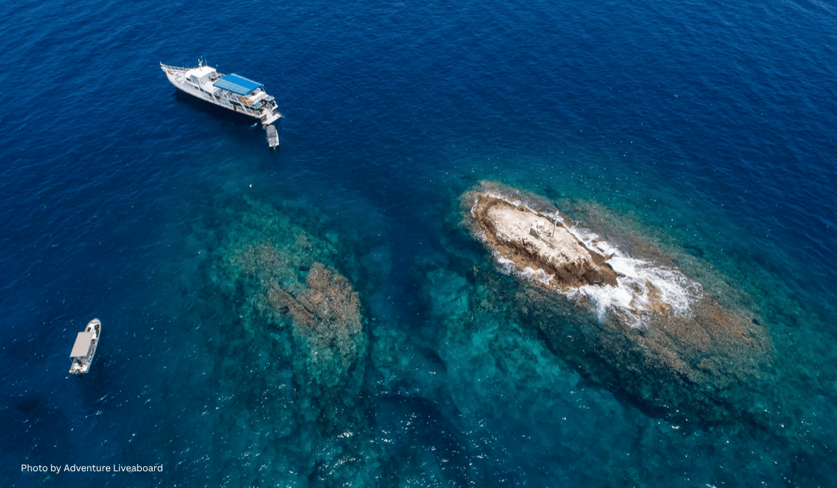 mexico liveaboards Aerial view of a white liveaboard dive boat and a small skiff anchored near a rocky reef in the deep blue waters of the Pacific Ocean during a Mexico dive safari.