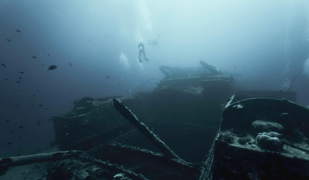 Two divers descending through hazy blue water onto a large, barely visible Red Sea shipwreck
