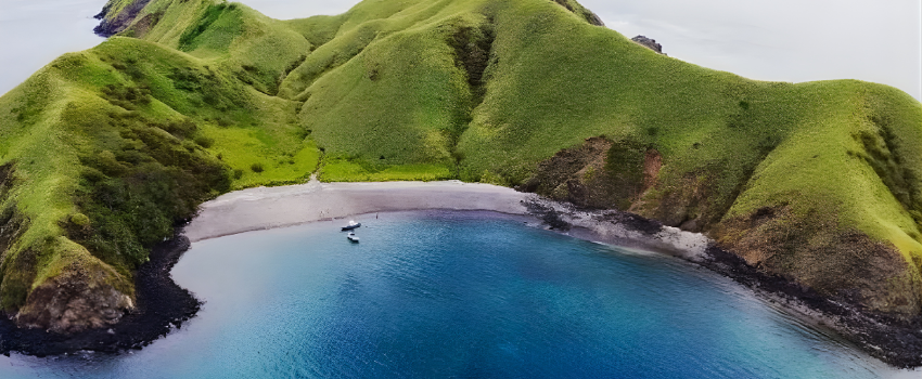 Secluded beach at Bat Islands, where to dive in Costa Rica for bull shark encounters at the Big Scare cleaning station, featuring vibrant green hills and two small boats anchored in clear, calm blue water.
