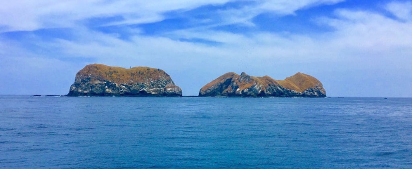 Two large, rocky, arid islands known as the Catalina Islands rising out of a calm blue ocean under a bright, hazy sky, among the best dive sites in Costa Rica for manta ray encounters.