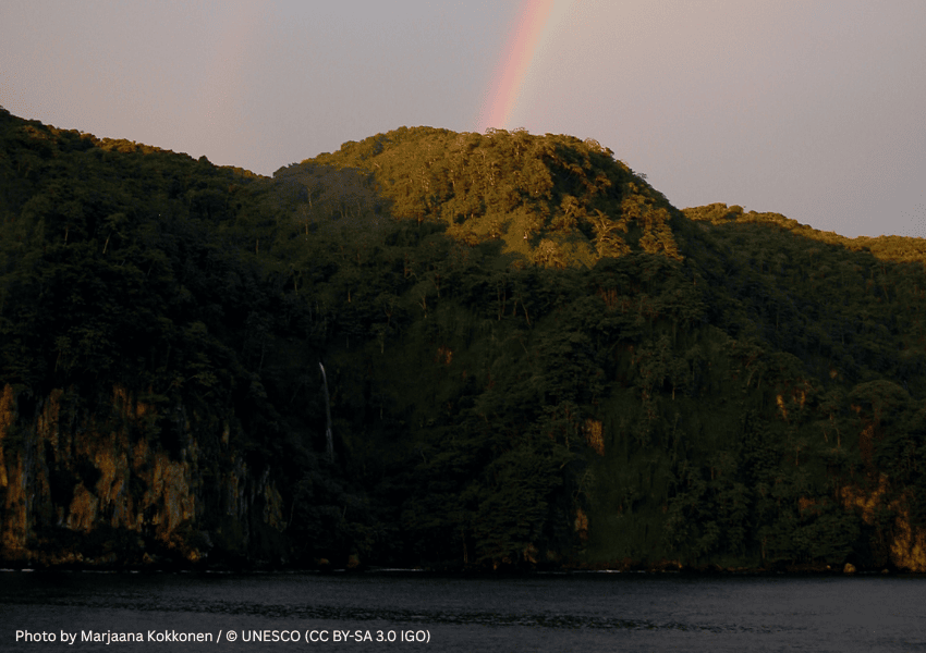 Lush green rainforest mountains and a waterfall under a rainbow at Cocos Island National Park.