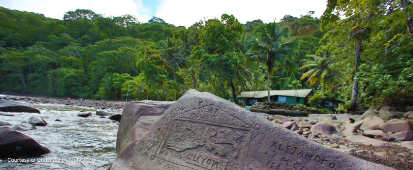 Historical stone carvings at Cocos Island featuring Jacques Cousteau's Alcyone logo with the ranger station in the background.