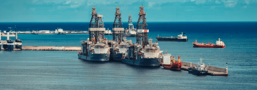 Industrial offshore drilling rigs and ships in a port, illustrating the rising global fuel costs that have led to liveaboard fuel surcharges in 2026