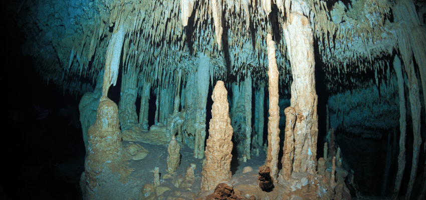 Dramatic limestone stalactites and stalagmites inside a crystal-clear freshwater cavern in the Tulum Cenotes, a world-class site for Mexico scuba diving and cavern exploration.