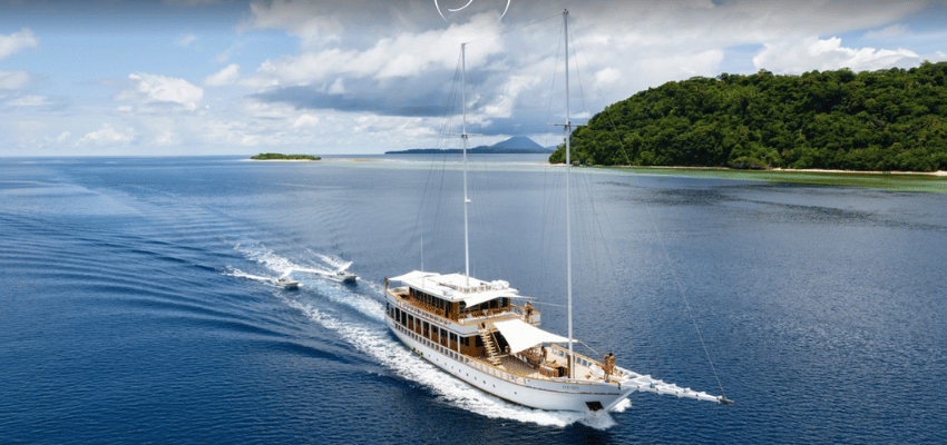 Fenides Liveaboard Indonesia Sleek, white minimalist luxury Phinisi Fenides anchored near a pristine Indonesian coral reef.