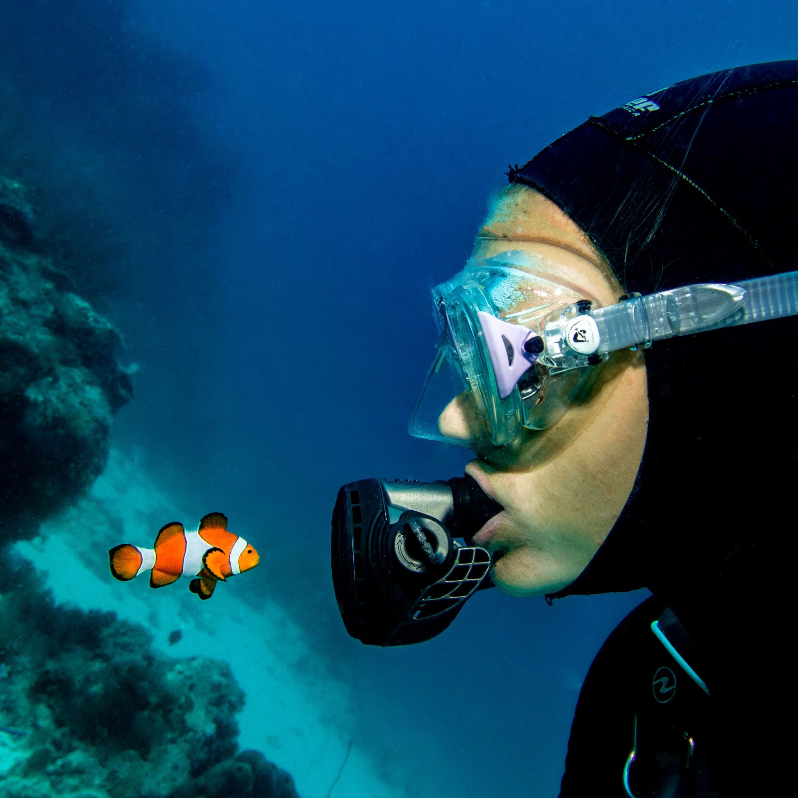 Female scuba diver underwater with clownfish during Women’s Dive Day